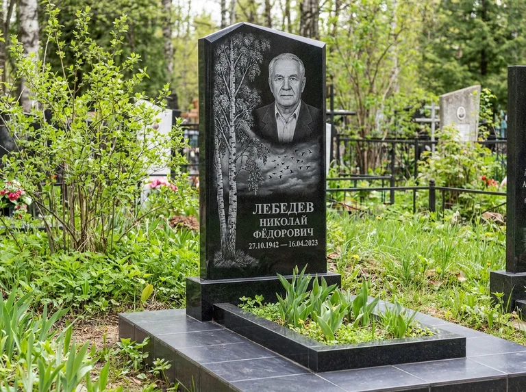 Памятник с гравировкой берёзы: вертикальная стела со скошенным верхом — берёза и стая птиц в небе, гранитный цоколь с тёмной плиткой, работа «Лебедев» в Томске