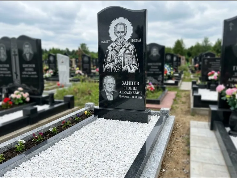 Памятник с гравировкой иконы: стела с крестообразным навершием — икона в резной рамке-киоте, газон без ограды, стриженая трава, работа «Раевская» в Томске