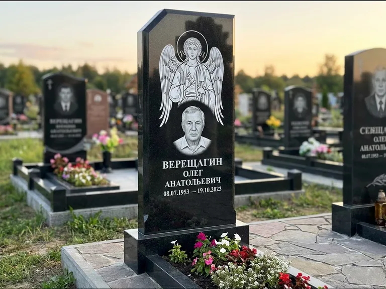 Памятник с гравировкой иконы: стела с резным навершием и нимбом в золоте — гравировка образа Спасителя, высокие разросшиеся туи полукругом, работа «Мельникова» в Томске