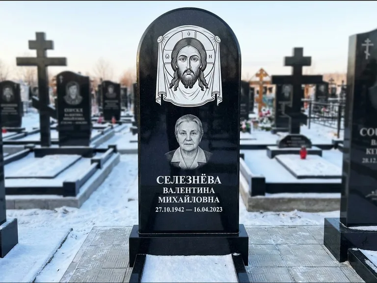Памятник с гравировкой иконы: небольшая скромная одиночная стела с именной иконой — золочёный нимб на образе, аккуратный участок с газоном, работа «Ковалёв» в Томске
