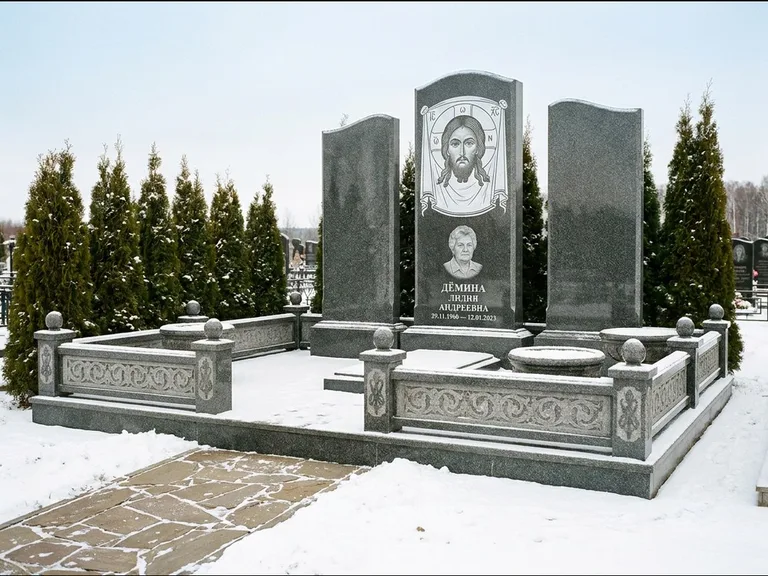 Памятник с гравировкой иконы: узкая вертикальная стела-пилон с ликом — икона в резной рамке-киоте, открытая лужайка без ограды, работа «Одинцов» в Томске
