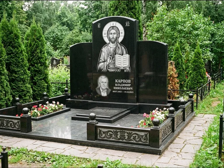Памятник с гравировкой иконы: широкая панорамная стела с золочёным нимбом — гравировка образа Матроны Московской, цветник с белыми хризантемами, работа «Мельникова» в Томске