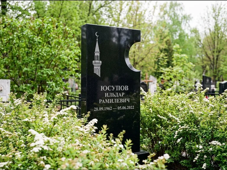 Мусульманский памятник с гравировкой мечети: стела с боковым вырезом в форме полумесяца — гравировка минарета с полумесяцем, низкие кусты спиреи в цвету, работа «Юсупов» в Томске